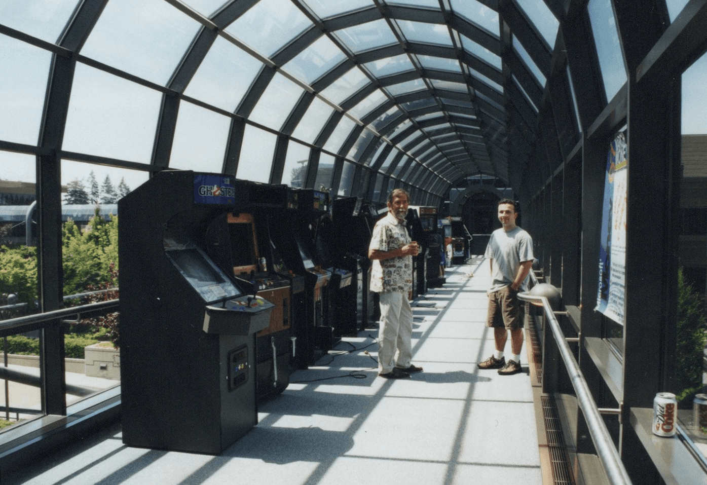 My dad and me standing beside arcade cabinets in the glass Microsoft skybridge between Buildings 17 and 18